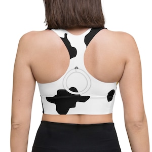 May include: A white and black cow print sports bra with a black racerback design. The bra has a small black ring on the back.