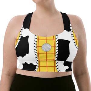 May include: A black and white cow print sports bra with a yellow and red grid pattern and a silver button. The bra has a racerback style.
