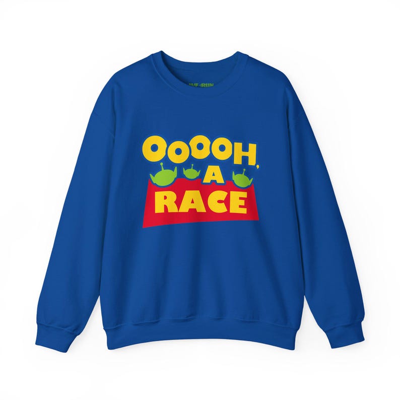 Puede incluir: Una sudadera azul real de cuello redondo con un estampado gr&aacute;fico que muestra el texto amarillo "OOOOOH, A RACE" sobre un rect&aacute;ngulo rojo. Tres peque&ntilde;as siluetas de alien&iacute;genas verdes de tres ojos se sit&uacute;an entre las palabras.