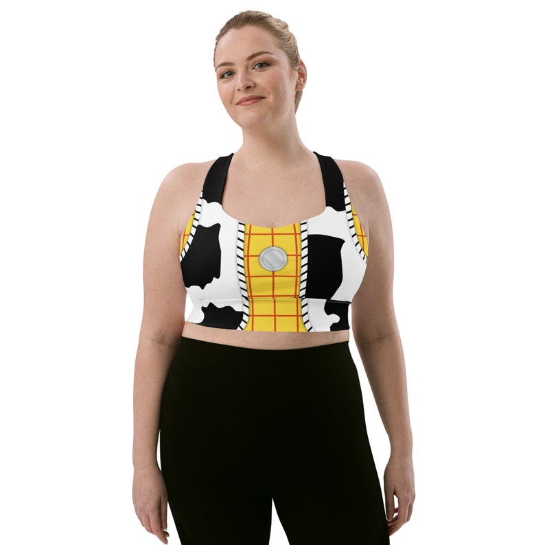 May include: A black and white cow print sports bra with a yellow and red grid pattern and a silver button. The bra has a racerback style.