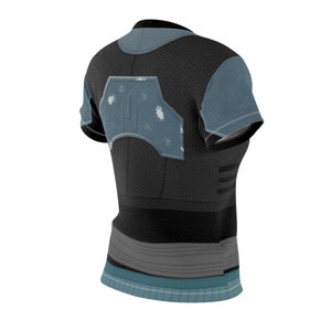 May include: A short-sleeved t-shirt in black and muted blue, featuring a textured pattern on the torso and sleeves. The back displays a large, weathered blue armor-like graphic panel with white distressed markings and a central vertical line detail.