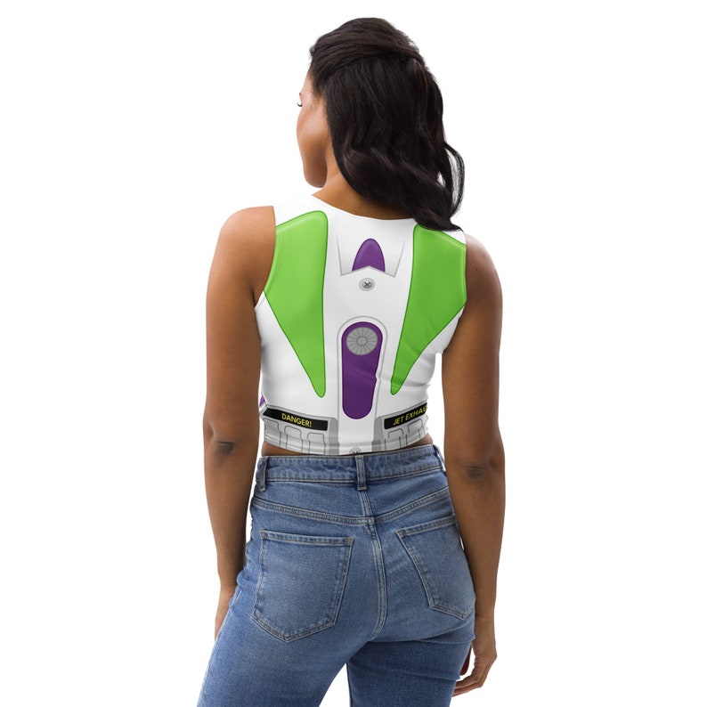 May include: White crop top with a Buzz Lightyear costume design. The top features green, purple, and gray accents, with the words "DANGER!" and "JET EXHAUST" printed on the bottom. The design is reminiscent of the character's space suit.