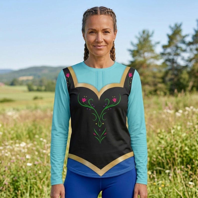 May include: A long-sleeve shirt featuring a black bodice with a gold-colored trim and a green floral pattern with pink accents. The sleeves and lower hem are light blue, and the shirt has a round neckline with a vertical stitched detail at the center.