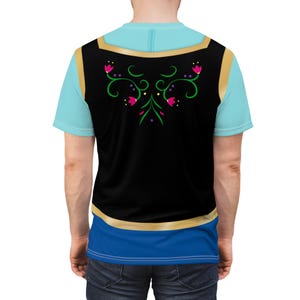 May include: A light blue t-shirt with a black vest overlay featuring a gold trim and floral design. The vest has a blue and gold trim. The shirt has a blue and gold trim at the bottom.