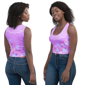 May include: A sleeveless lavender crop top featuring a scalloped white neckline detail and a vibrant floral pattern in shades of pink, purple, and blue. The garment is shown from both the front and back views, paired with dark blue denim jeans.