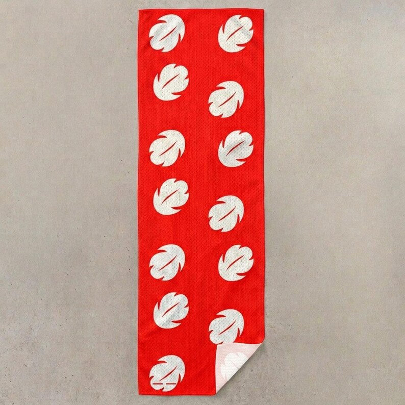 Op de afbeelding: Een rode rechthoekige handdoek met een herhaald patroon van witte, gestileerde bladvormen. De handdoek is gemaakt van een gaasachtig materiaal en heeft een opgevouwen hoek, waardoor een witte onderkant zichtbaar is.