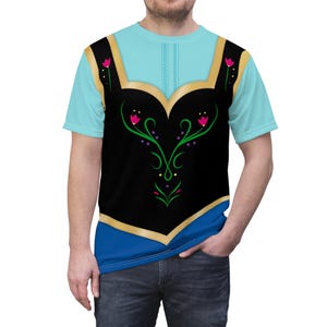 May include: A light blue t-shirt featuring a black bodice design with gold trim and floral accents. The shirt has a blue neckline and sleeves, and is worn by a person.