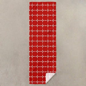 Pu&ograve; includere: Un asciugamano rettangolare rosso con un motivo geometrico bianco. Il motivo &egrave; composto da forme a diamante bianche e punti disposti a griglia. L'angolo inferiore dell'asciugamano &egrave; piegato, rivelando un lato inferiore bianco.
