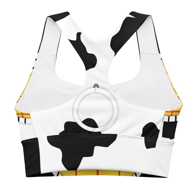 May include: A white and black cow print sports bra with yellow and red accents. The bra has a racerback style and a ring on the back for adjusting the straps.