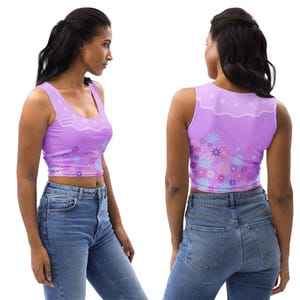 May include: A sleeveless lavender crop top featuring a white scalloped neckline detail and a vibrant floral pattern in shades of blue, purple, and pink across the bottom hem, paired with blue denim jeans shown from side and back views.