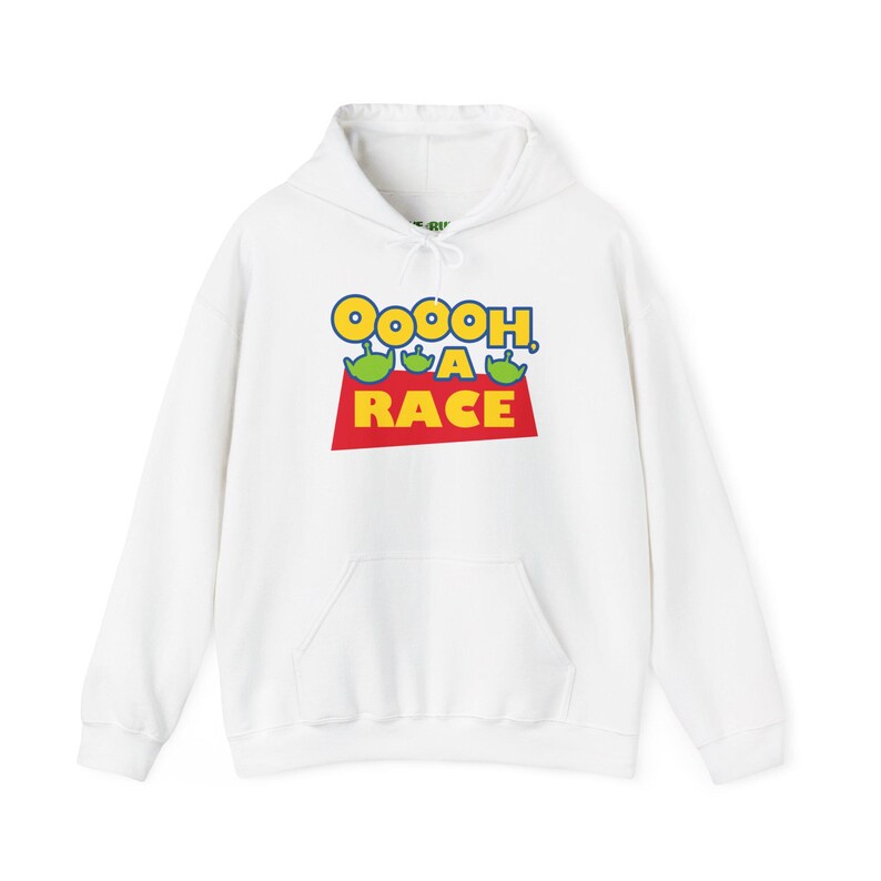 Puede incluir: Una sudadera blanca con capucha y manga larga que presenta un estampado gr&aacute;fico en el pecho. El dise&ntilde;o incluye el texto "OOOOH, A RACE" en letras azules y amarillas, acompa&ntilde;ado de tres peque&ntilde;os personajes alien&iacute;genas verdes sobre un trapecio rojo.