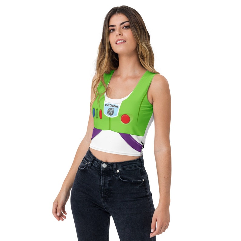 May include: A white crop top with a green Buzz Lightyear costume design. The top features a green chest plate with the words "SPACE COMMAND" and colorful buttons. The design includes purple accents and a scoop neckline.