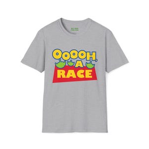 Puede incluir: Una camiseta gris jaspeado de manga corta con un estampado gr&aacute;fico que incluye el texto Ooooh, A RACE en letras amarillas y rojas. Tres cabezas de alien&iacute;genas verdes se sit&uacute;an sobre la palabra RACE. La etiqueta interior dice WE RUN FOR FUN.