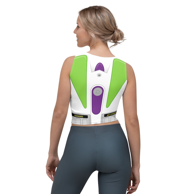 May include: White crop top with a Buzz Lightyear costume design. The top features green, purple, and gray accents, with the words "DANGER!" and "JET ENGINE" printed on the bottom. A fun and unique piece of apparel.