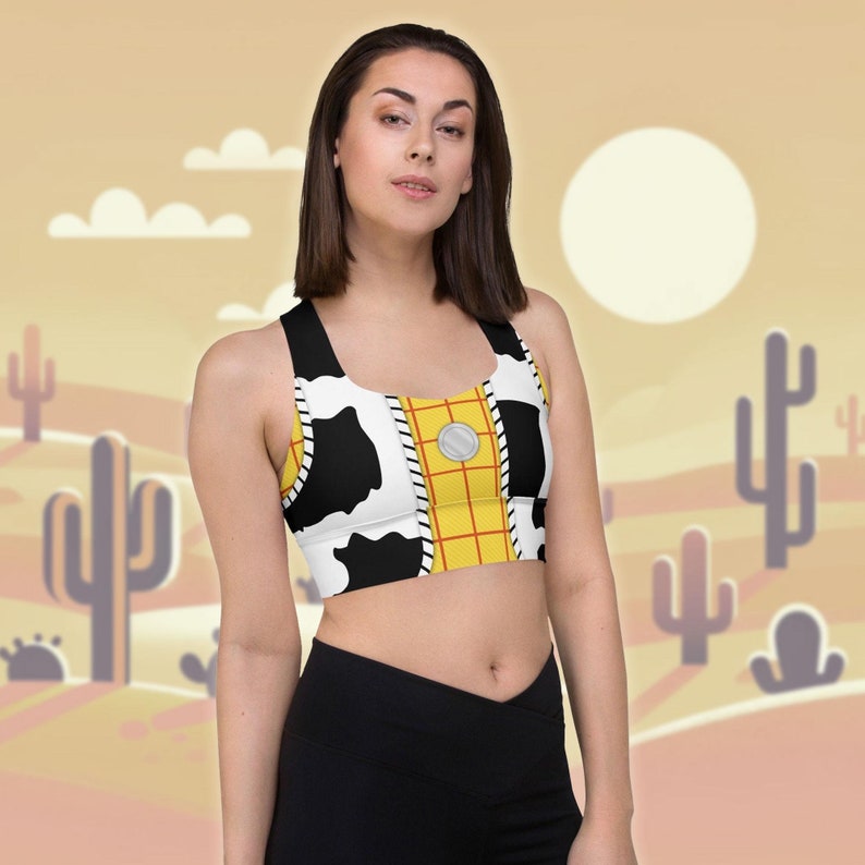May include: A black and white cow print sports bra with a yellow and red plaid pattern on the front. The bra has a scoop neck and racerback style.