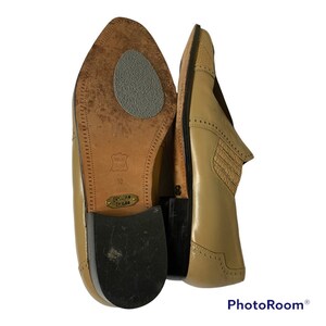 May include: A pair of tan leather dress shoes with a pointed toe and decorative perforations. The soles are visible, showing the size 10 and the brand name. The shoes have a classic, formal style.