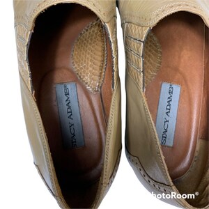 May include: Tan leather Stacy Adams shoes. The shoes have a textured design on the top and a perforated pattern along the edges. The interior features a brown insole with the Stacy Adams logo.