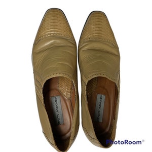 May include: A pair of Stacy Adams tan leather dress shoes. The shoes have a textured, reptile-like design on the toe and side panels. The shoes are a slip-on style with a low heel and a leather sole.