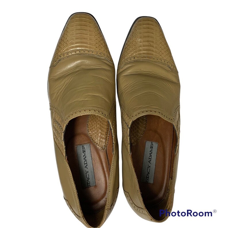 May include: A pair of Stacy Adams tan leather dress shoes. The shoes have a textured, reptile-like design on the toe and side panels. The shoes are a slip-on style with a low heel and a leather sole.