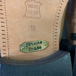 May include: Close-up of the sole of a shoe. The sole is tan leather with the words "GENUINE LEATHER" embossed. A metal tag reads "Genuine Snake". The number "10" is stamped on the leather.
