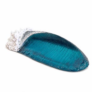 May include: A sculptural representation of a breaking ocean wave made of translucent deep blue resin. The crest of the wave features textured, opaque white foam detailing, while the main body of the wave displays a smooth, glossy finish.