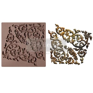 May include: A brown silicone mold with a corner design of ornate floral scrollwork. Next to it is a cast piece in bronze and gold tones, showcasing the detailed relief pattern. The design is suitable for crafts and decorative projects.