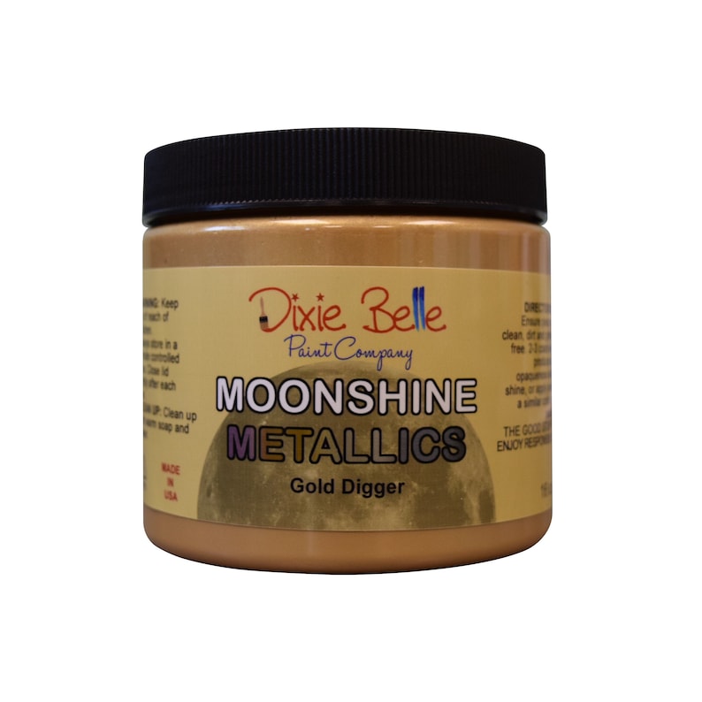 Pode incluir: Um frasco de vidro de tinta Moonshine Metallics da Dixie Belle na cor Gold Digger. O frasco tem uma tampa preta e um r&oacute;tulo branco com o logotipo da Dixie Belle e as palavras "Moonshine Metallics" e "Gold Digger".
