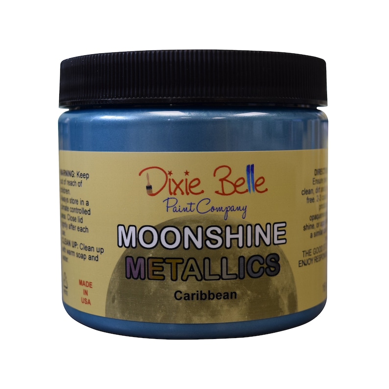 Pode incluir: Um frasco de vidro de tinta Moonshine Metallics da Dixie Belle na cor Caribe. O frasco tem uma tampa preta e um r&oacute;tulo amarelo com o logotipo da Dixie Belle e as palavras "Moonshine Metallics" e "Caribe".
