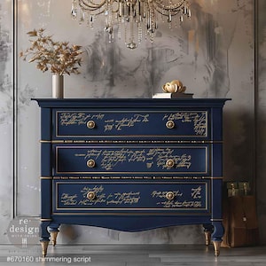 May include: A navy blue dresser with three drawers, each decorated with gold script writing. The dresser has gold accents on the drawer pulls and along the top and bottom edges of the drawers. The dresser is sitting on a wooden floor.