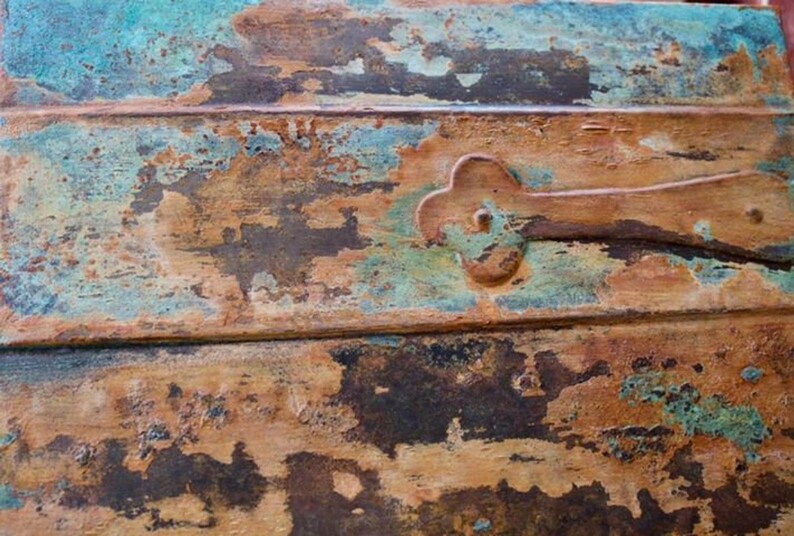 May include: Close-up of a wooden surface with a distressed, weathered look. The surface is painted in shades of blue, green, brown, and rust. A metal hinge is attached to the surface.