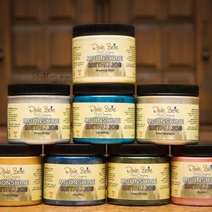 Pode incluir: Oito garrafas de tinta Moonshine Metallics da Dixie Belle em v&aacute;rias cores, incluindo ouro, prata, cobre e verde. As garrafas est&atilde;o dispostas em duas filas de quatro, com o logotipo da Dixie Belle e o nome do produto vis&iacute;vel em cada garrafa.