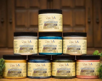 May include: Eight bottles of Dixie Belle Moonshine Metallics paint in various colors, including gold, silver, copper, and green. The bottles are arranged in two rows of four, with the Dixie Belle logo and product name visible on each bottle.