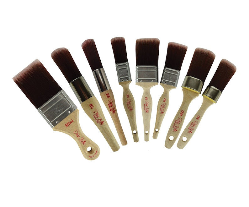 May include: A set of eight paint brushes with wooden handles and red lettering that says "The Dixie Belle". The brushes are arranged in a semi-circle with the handles pointing towards the center. The brushes are different sizes and have different lettering on the handles, including "Mini", "RL", "RS", "PW", "OW", and "GS".