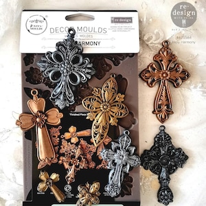 May include: A silicone mold for making decorative crosses. The mold is shown with several finished crosses in different colors, including gold, silver, and black. The mold is labeled "Decor Moulds Holy Harmony".