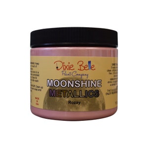 Pode incluir: Um frasco de vidro de tinta met&aacute;lica rosa com a etiqueta "Dixie Belle Paint Company Moonshine Metallics Rozay".