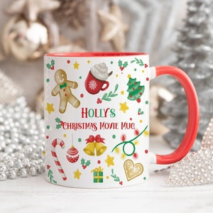 May include: White ceramic mug with a red rim and handle. The mug features a Christmas movie theme with illustrations of a gingerbread man, a Christmas tree, candy canes, baubles, bells, and a gift box. The text "Holly's Christmas Movie Mug" is printed on the mug.