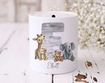 May include: White ceramic money box with a wooden letter E, a giraffe, a monkey, a tiger, and an elephant. The name Elliott is written below the animals.