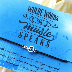 Peut inclure: Un bracelet en cordon noir avec un charme en argent en forme de cl&eacute; de sol. Le bracelet est livr&eacute; avec une carte bleue sur laquelle est inscrit "L&agrave; o&ugrave; les mots &eacute;chouent, la musique parle".