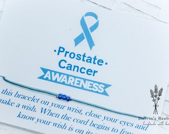Peut inclure: Un bracelet bleu en cordon avec un petit cordon bleu. La carte indique "Prostate Cancer AWARENESS" et "Attachez ce bracelet à votre poignet, fermez les yeux et faites un vœu. Lorsque le cordon commence à s'effilocher, sachez que votre vœu est en route." La carte contient également un petit graphique de fleur de lavande et le texte "Dalvin's Baubles fait à la main avec amour."