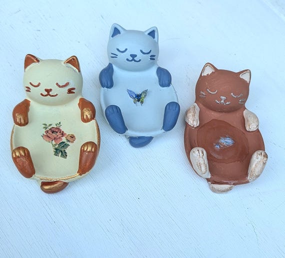 A sculptural cat figurine doubles as a ring holder — the butterfly detail makes it feel like a tiny piece of whimsical ceramic art, not just a dish.