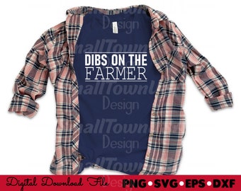 May include: A navy blue t-shirt with white text that reads "DIBS ON THE FARMER". The t-shirt is layered over a pink and black plaid shirt.