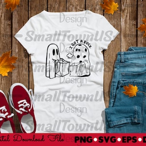 Peut inclure: Un t-shirt blanc avec une illustration en noir et blanc de deux fantômes. Un fantôme tient un sac qui dit "J'ai un rocher". Le t-shirt est sur une surface en bois avec un jean bleu et des feuilles d'automne.