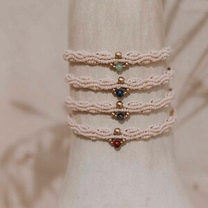 May include: Five delicate bracelets made of white cord with a single gemstone bead in each. The beads are green, blue, dark blue, and red.