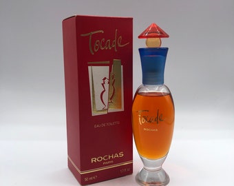 May include: A red box with gold lettering that reads "Tocade" and "Rochas Paris" with a 1.7 fl oz bottle of Tocade Eau de Toilette by Rochas. The bottle is clear glass with a red and gold cap.
