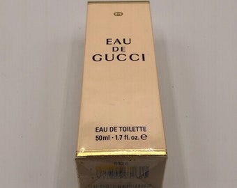 May include: A white and gold box with the text "Eau de Gucci" and "Eau de Toilette 50ml - 1.7 fl. oz. e" printed on it.