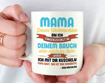Puede incluir: Taza de cerámica blanca con la palabra "MAMA" en azul y texto en alemán. La taza tiene un asa y la sostiene una persona. El texto incluye "Dieses Weihnachten BIN ICH EINGEKUSCHELT IN DEINEM BAUCH".