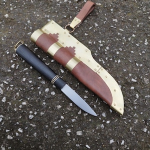 May include: A black-handled knife with a brass-trimmed handle and a silver blade. The knife is in a brown leather sheath with brass accents and a leather strap.