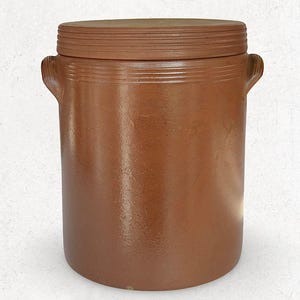 May include: A brown stoneware crock with a matching lid. The cylindrical container has two small handles and horizontal ridges near the top. The lid also has ridges. The crock is a warm, earthy tone.