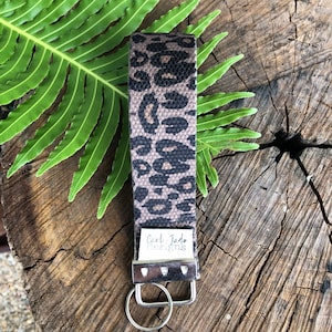 May include: A brown and black leopard print key chain with a silver key ring and a white tag that says "Carl Jade Designs".