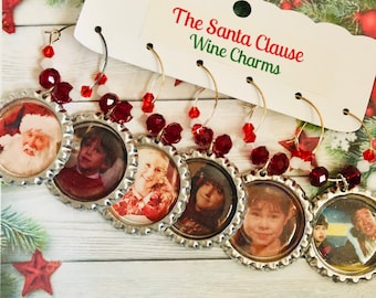 May include: Set of six wine charms featuring images from "The Santa Clause" movie. Each charm is made from a bottle cap with a picture inside, adorned with red beads and gold-colored wire. The tag reads "The Santa Clause Wine Charms".